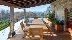 Una mesa de madera con sillas en un balcón con pared de piedra y plantas en macetas.