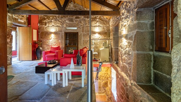 Interior con paredes de piedra, una escalera de madera, asientos rojos y una mesa blanca.
