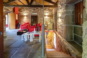 Un intérieur aux murs de pierre, avec un escalier en bois, des sièges rouges et une table blanche.