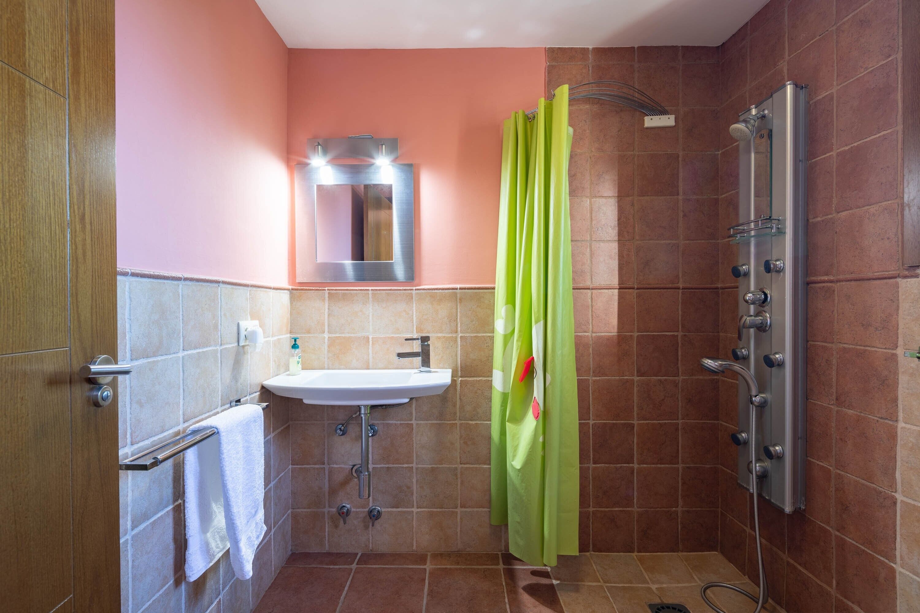 A bathroom with a sink, mirror, shower, and a green shower curtain.