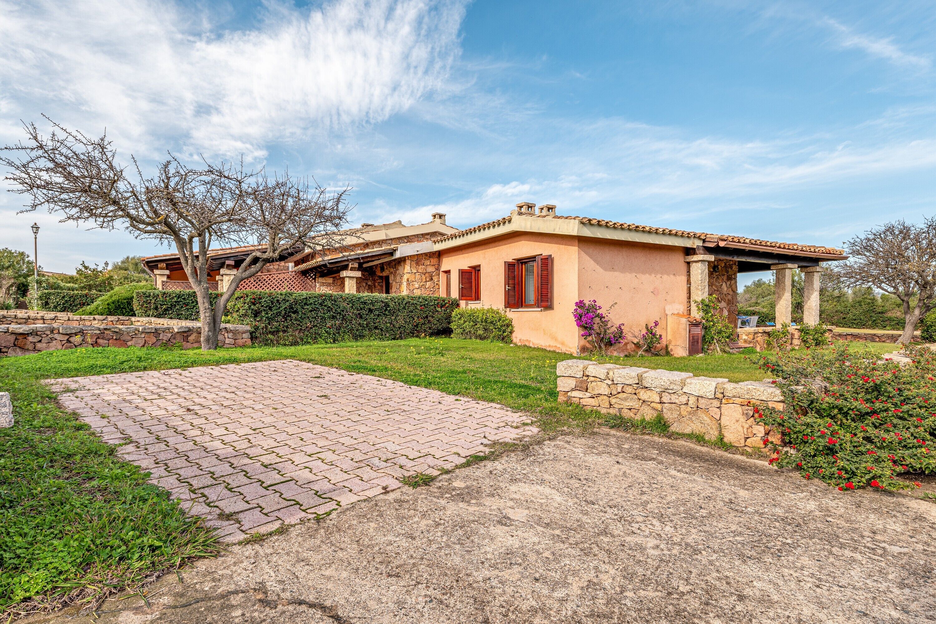 A house with a paved driveway, stone wall, and a well-maintained garden.