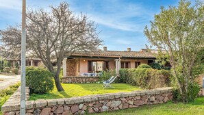 A house with a stone wall, a lawn, and a chair.
