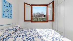A bedroom with a bed, a window, a wardrobe, and a wall with a painting.