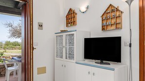 A room with a television, cabinets, a table with chairs, and a view of the outdoors.