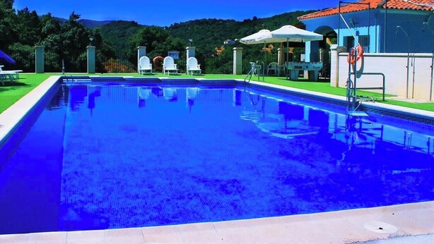 Une piscine rectangulaire à l’eau d’un bleu limpide, entourée d’une pelouse verdoyante, de chaises longues blanches et de parasols.