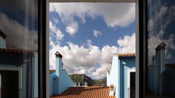 A view through a window of a building with a tiled roof and blue walls, with a mountain and cloudy sky in the background.