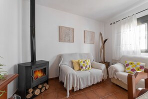 A cozy living room with a wood-burning stove, two sofas, and a large window with curtains. - Holiday Home 'La Casa Del Bosque' with Mountain Views, Balcony & Wi-Fi (Júzcar)
