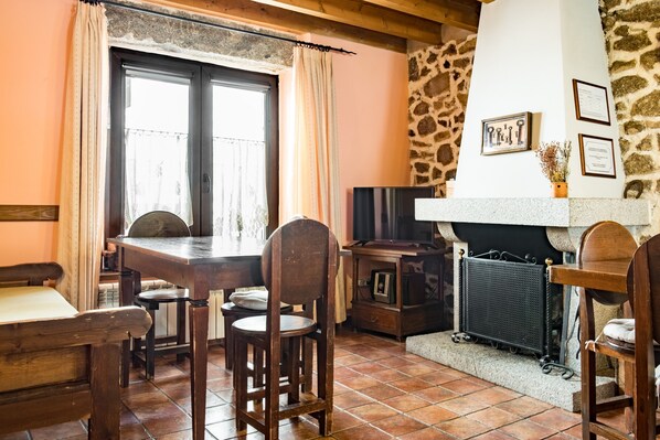 Un'accogliente zona pranzo con un tavolo e sedie in legno, un camino, una parete in pietra e un televisore.