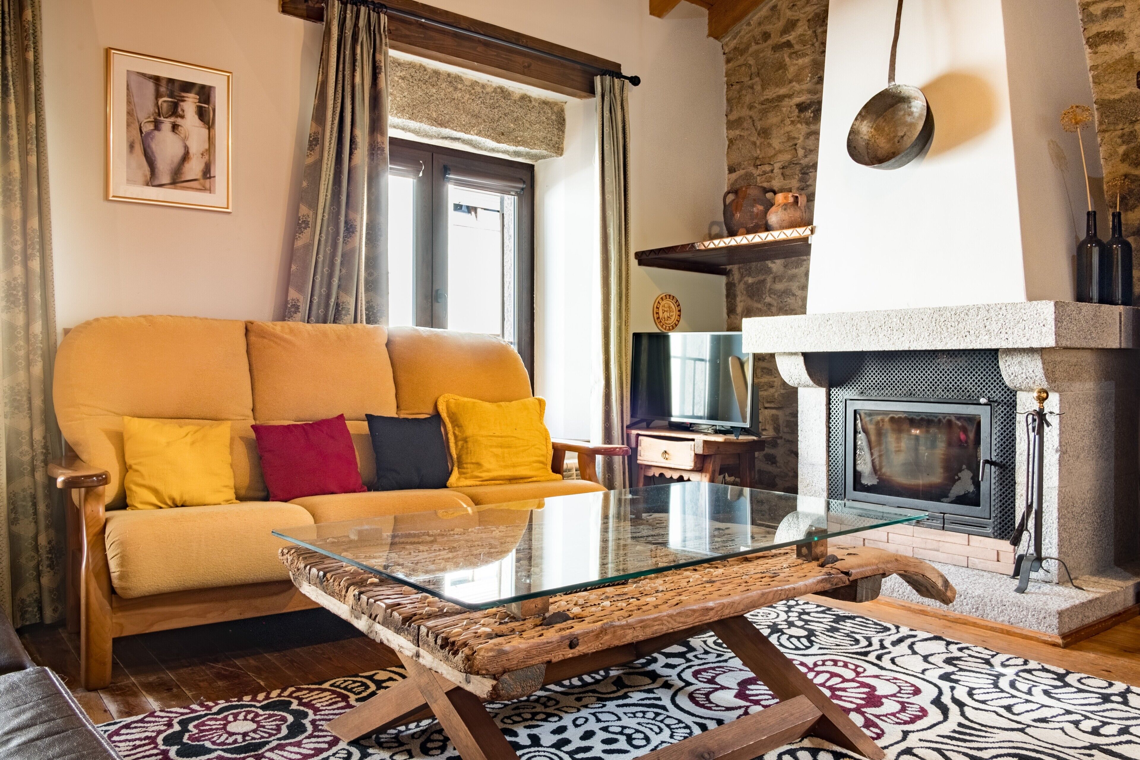 Ein Wohnzimmer mit Sofa, Glastisch, gemustertem Teppich, Kamin und Steinwand.