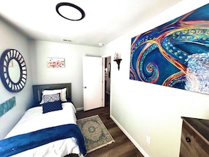 Una camera da letto con un letto, uno specchio, una porta, un quadro a parete e un tappeto.