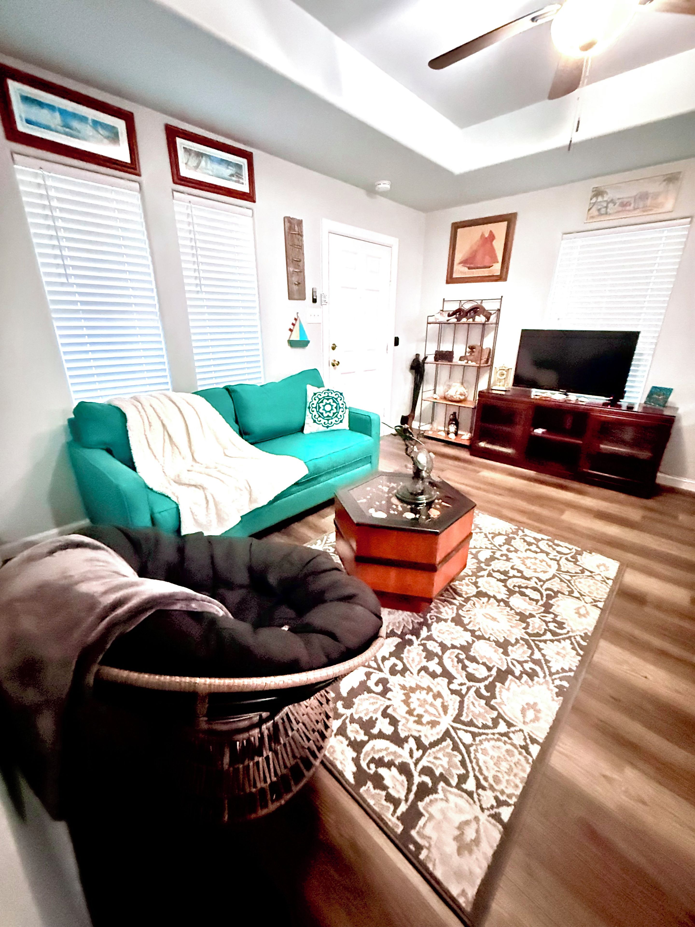 A living room with a teal sofa, a black chair, a coffee table, and a television.