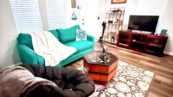 A living room with a teal sofa, a black chair, a coffee table, and a television.