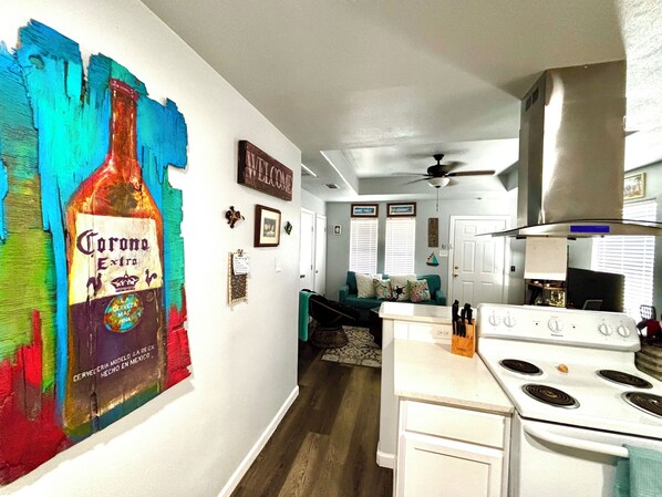 A kitchen with a white stove, a ceiling fan, and a colorful wall mural of a beer bottle.