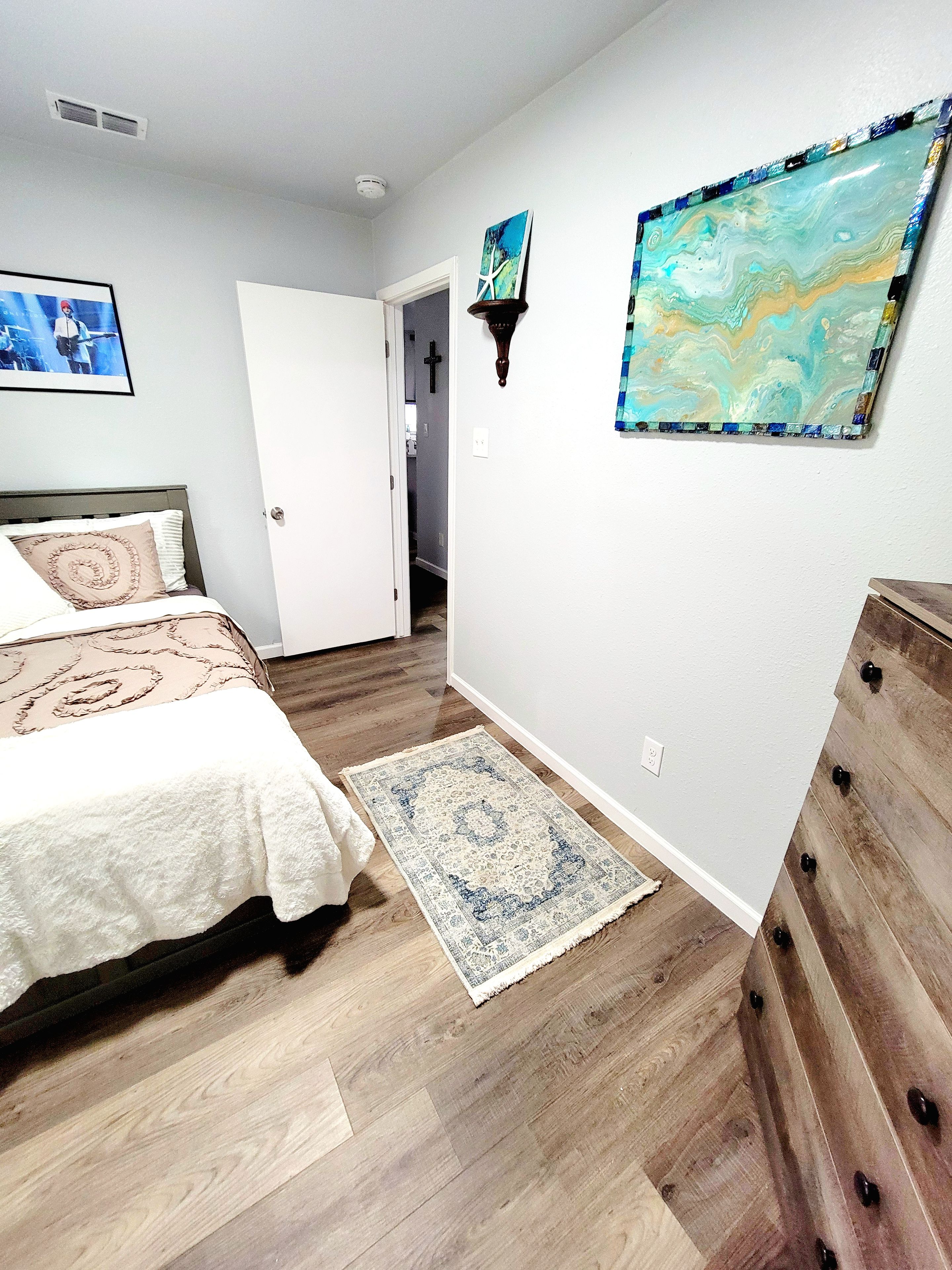 Un dormitorio con una cama, un aparador de madera, un tapete y dos cuadros colgados en la pared.