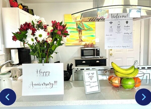 A kitchen counter with a 'Happy Anniversary!!!' sign, a vase of flowers, a 'Welcome!' sign, a Wi-Fi sign, and a fruit basket. - PRIME LOCATION IMMACULATE COZY GETAWAY MINUTES FROM BEACH &DOWNTOWN (Corpus Christi)