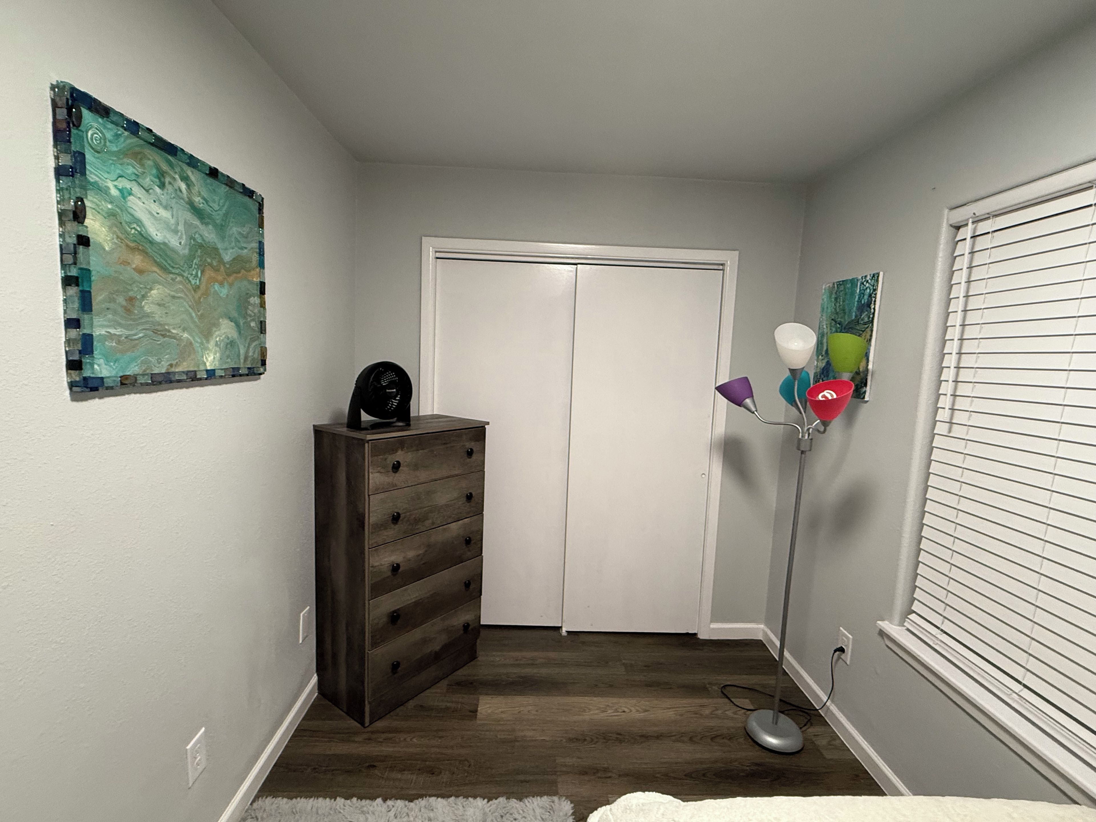 A room with a wooden dresser, a door, a floor lamp, and a wall art piece.