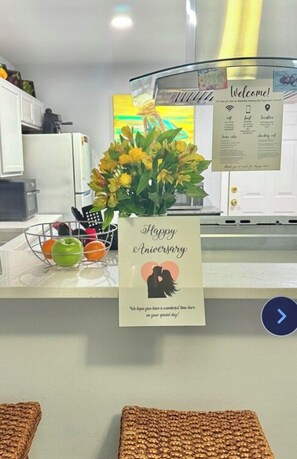 Un área de recepción con un cartel de bienvenida, un jarrón de flores y una tarjeta que dice "Feliz Aniversario".