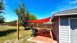 Ein Hinterhof mit Patio, einem roten Sonnensegel, einem Grill sowie einem Tisch und Stühlen.