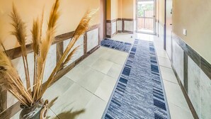Un pasillo con alfombra azul estampada, barandilla de madera y un florero con plumas de pampa.