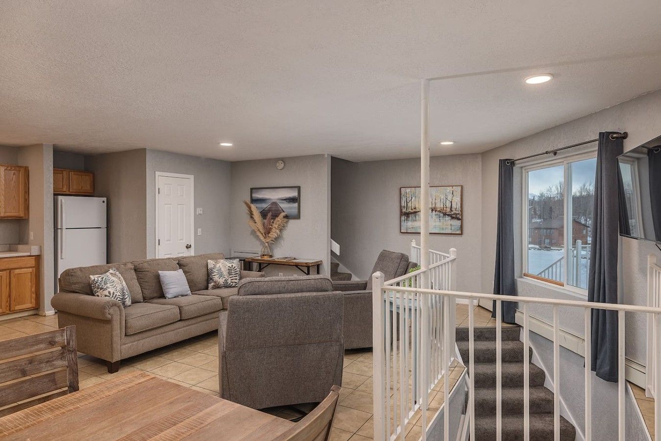 A modern living room with a sofa set, a dining table, and a staircase leading to an upper level.