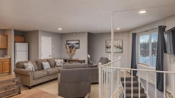 A modern living room with a sofa set, a dining table, and a staircase leading to an upper level.