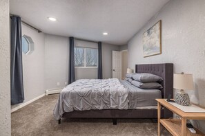 Un dormitorio con una cama, una mesita de noche, una lámpara, una puerta y una ventana.