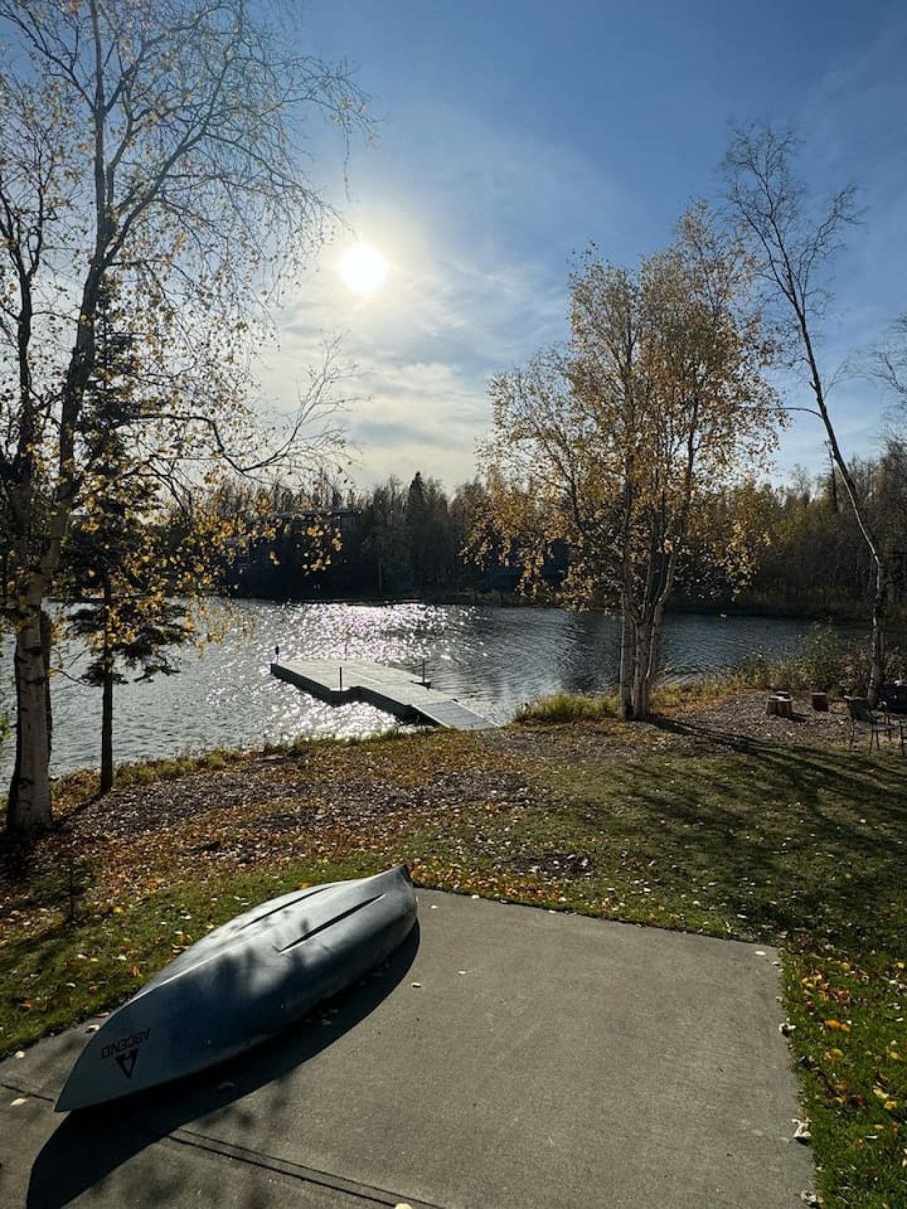 A lakeside view with a kayak, trees, and a clear sky.