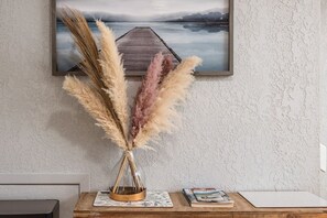 Un cuadro de paisaje enmarco, un florero con plumas de pampa y un libro sobre una mesa de madera.