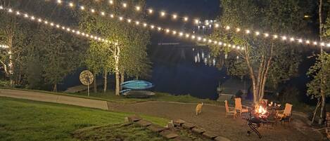 Un espace extérieur aménagé pour la nuit, avec des guirlandes lumineuses, un foyer et des sièges.