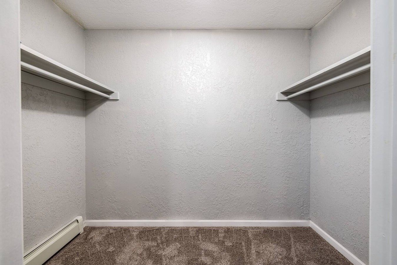 A small, enclosed space with white walls and a carpeted floor, featuring two white shelves on the walls.