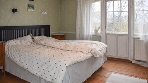 A bedroom with a bed, a nightstand, a window with curtains, and a small potted plant on the windowsill.