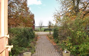 A paved pathway leading to a building, surrounded by dense foliage and a clear sky.