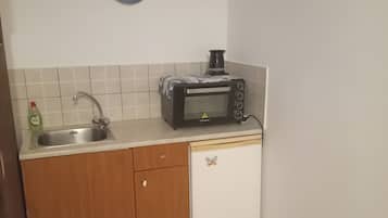 Een koelkast, een oven, een kookplaat, kookgerei, borden en bestek
