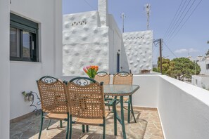 Un balcón con mesa y sillas, un jarrón con flores y una pared blanca con textura.