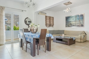 Comedor con una mesa, sillas y un jarrón con flores. Hay un sofá y un cuadro en la pared.