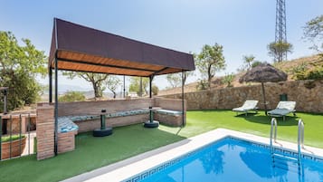 Une piscine agrémentée d’une pergola, d’un mur en pierre et d’une pelouse avec des chaises longues.