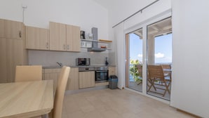 A compact kitchen with modern appliances, a dining area with a table and chairs, and a sliding glass door leading to a balcony with a view. - Nice apartment in Lukovo with house sea view (Lukovo)