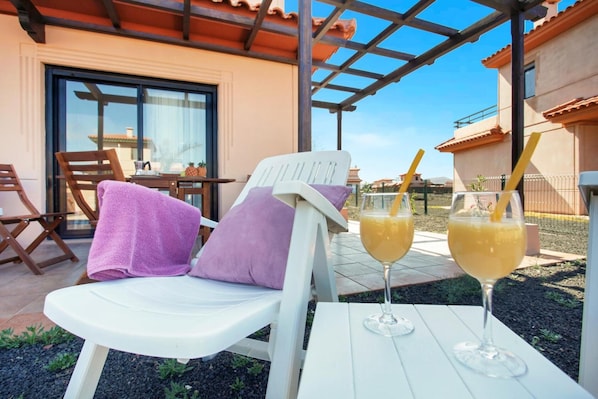 A patio with a white chair, a table, and two glasses of orange juice.