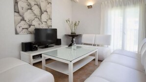 Ein modernes Wohnzimmer mit Flachbildfernseher, weißen Sofas, einem Glastisch und einem an der Wand hängenden Kunstwerk.
