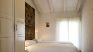 Ein Schlafzimmer mit Bett, Sessel, Kleiderschrank und einem Fenster mit Vorhängen.