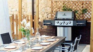 Ein Essbereich im Freien mit einem Holztisch, gedeckt für eine Mahlzeit, einem Grill und einer Steinwand im Hintergrund.