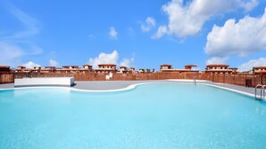 A swimming pool with a wooden fence, clear blue sky, and buildings in the background. - Vacation 'Bonita Lajares 3' with Shared Pool, Private Terrace and Wi-Fi (Lajares)