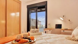 A hotel room with a bed, a desk, a chair, a tray with croissants and a cup, and a window with a view of a building. - Vacation 'Bonita Lajares 3' with Shared Pool, Private Terrace and Wi-Fi (Lajares)