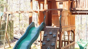 A wooden play structure with a slide and climbing wall.