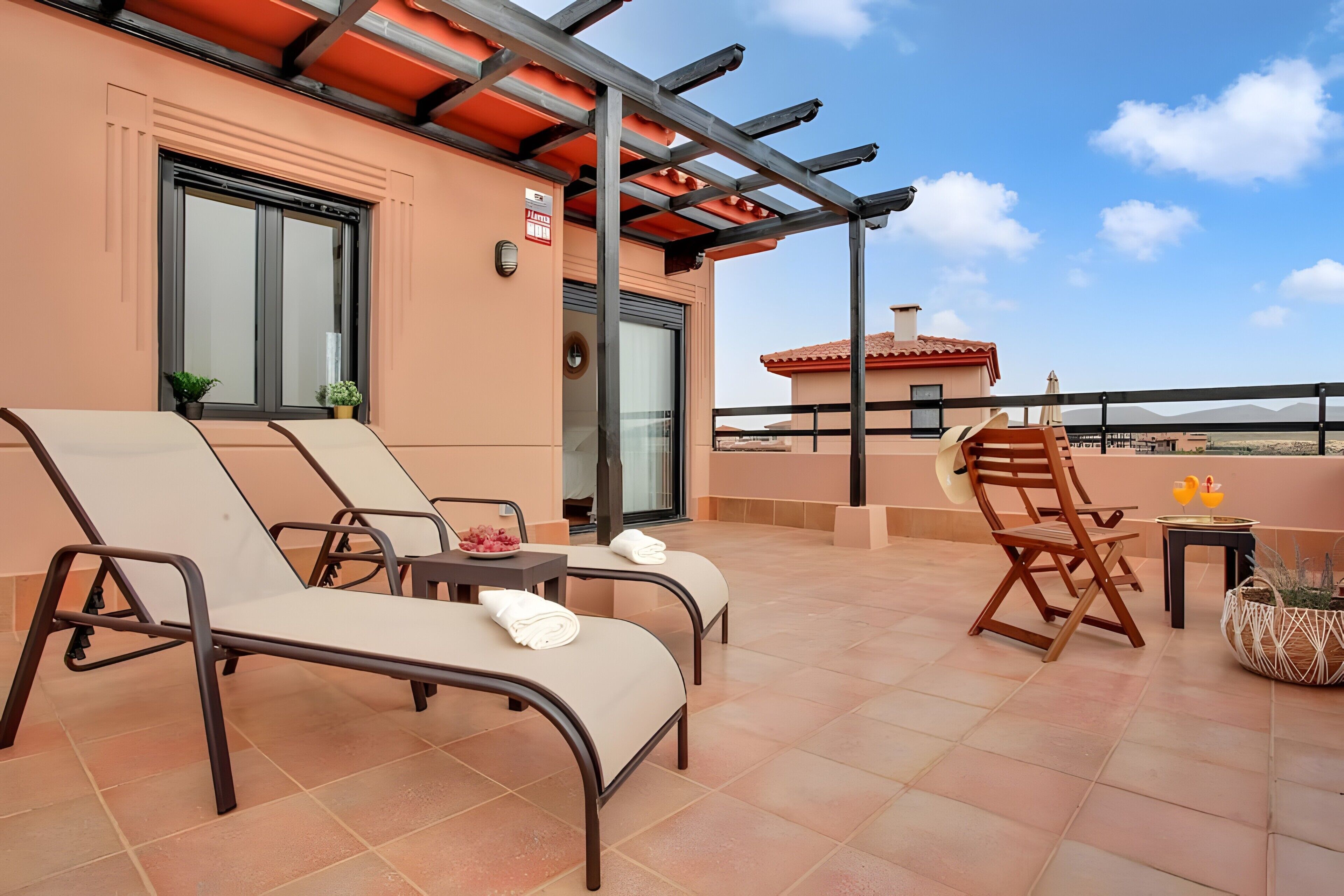 A rooftop terrace with lounge chairs, a table, and a chair, with a clear view of the surrounding landscape.