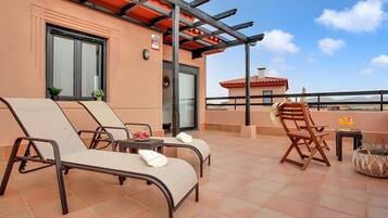 A rooftop terrace with lounge chairs, a table, and a chair, with a clear view of the surrounding landscape.