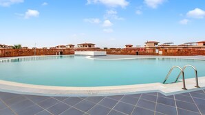 A swimming pool with a wooden fence, a tiled deck, and a clear blue sky.