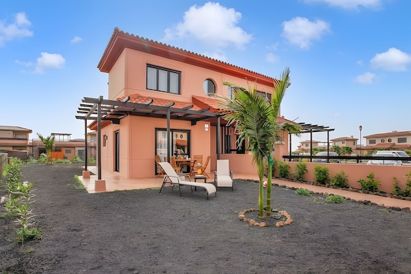 A two-story building with a patio area, outdoor seating, and a palm tree.