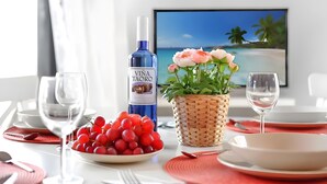 A dining table set with plates, glasses, a bottle of wine, a bowl of grapes, and a potted plant.