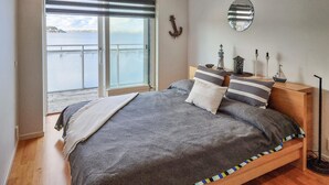 A bedroom with a large bed, a view of the sea through a sliding door, and nautical decor including an anchor and ship models. - Beach front home in Rönnäng with sauna (Rönnäng)